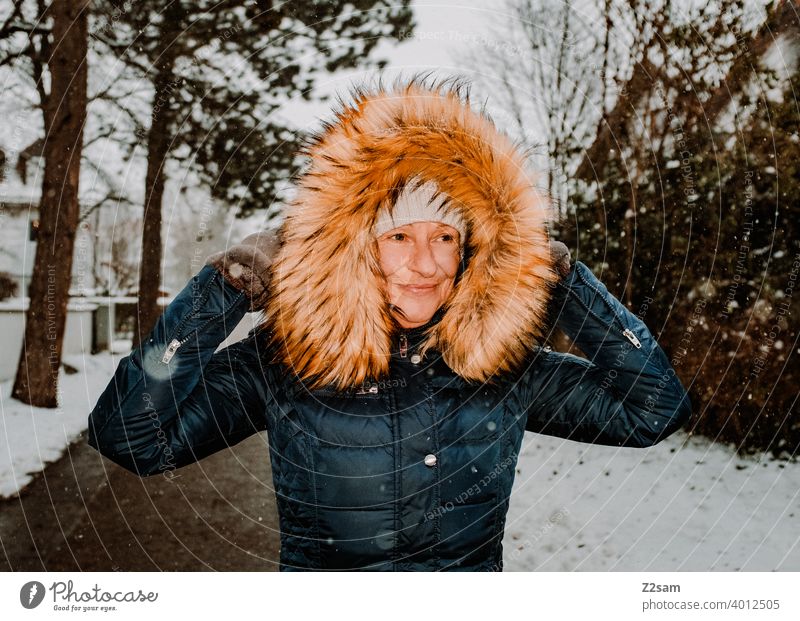Frau spaziert bei Schneefall durch die Straßen spaziergehen walk winterwalk mantel kunstpelz lachen lächeln wärme schneefall kälte weiß jacke bäume dorf freude