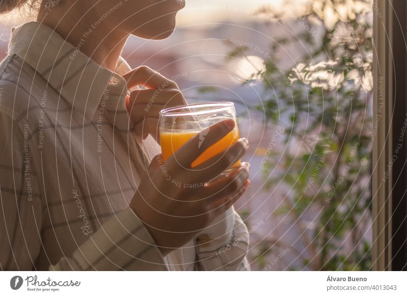Young woman enjoying a freshly squeezed orange juice at home. young drinking glass pretty crystal morning early next to window freshness light half-covered sun