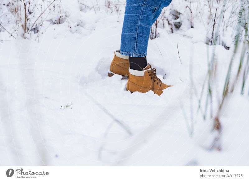 Feet in yellow, orange boots, legs in blue jeans in snow. Hike, outdoor recreation. Girl, woman walks in beautiful winter forest hike feet young walking girl