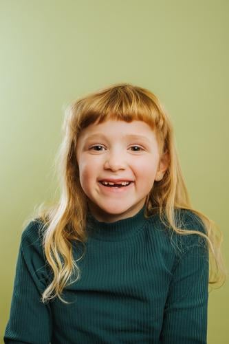 portrait of laughing blonde girl against green background bangs blond hair casual clothing child childhood colored background cute daughter emotion front view