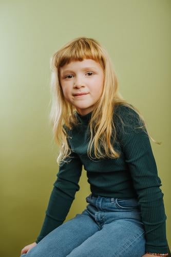 portrait of cute blonde girl against green background bangs blond hair casual clothing child childhood colored background emotion hairstyle indoors innocence