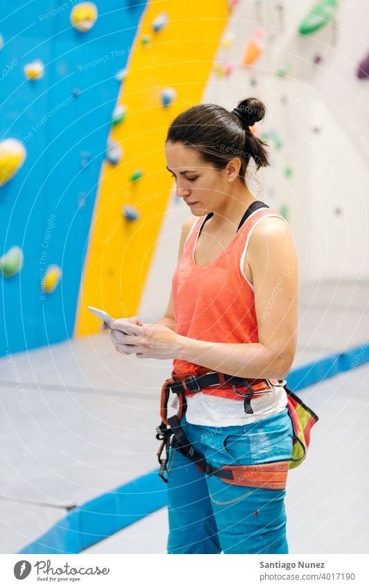 Rock climber woman looking at smartphone. sport climbing training rock wall leisure athlete technology mobile phone cellphone activity fitness indoor exercise