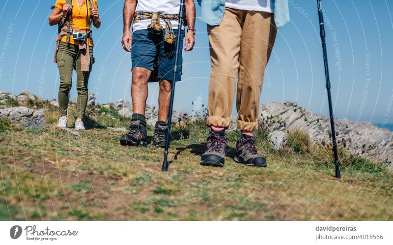 Three people practicing trekking outdoors unrecognizable group hikers mountain boots legs low section trekking sticks woman countryside landscape nature journey