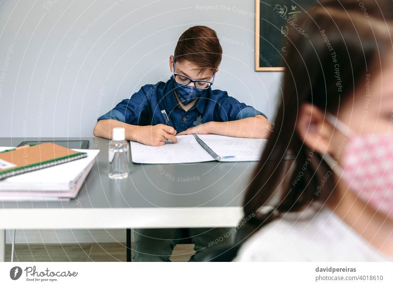 Boy with face mask writing at school boy student classroom new normal coronavirus safety people epidemic education health prevention young girl covid-19