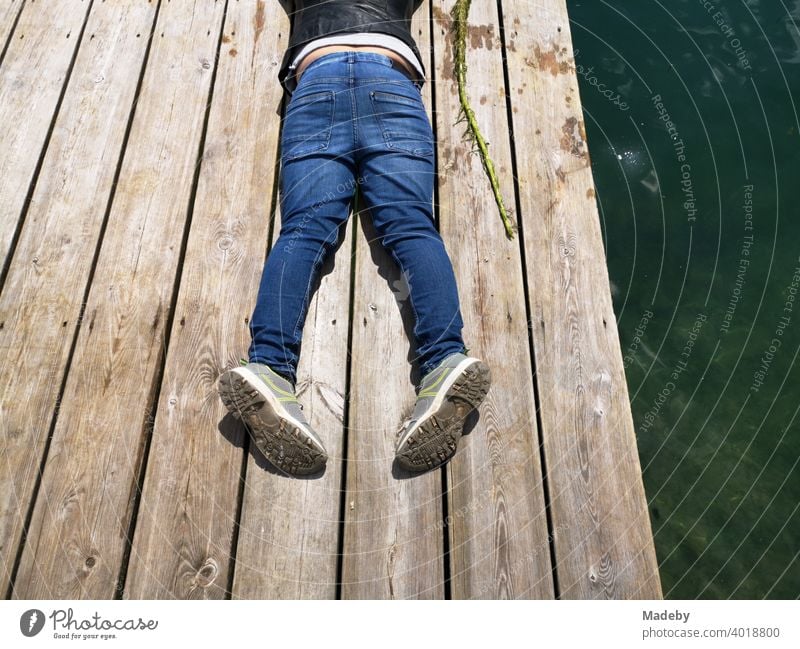 Boy in blue jeans on a landing stage made of rustic wood at the Lippesee in summer in Paderborn in East Westphalia-Lippe wooden walkway jetty bathing jetty