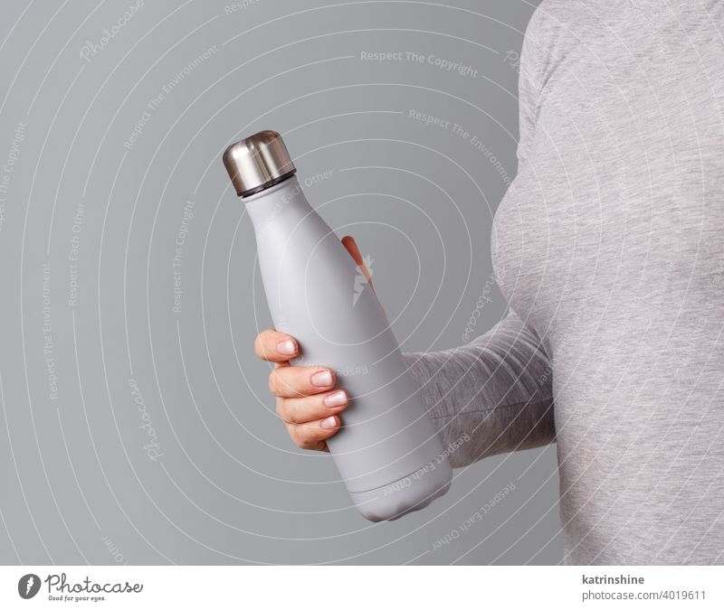 Woman in grey tee holding grey insulated bottle on grey background reusable hand woman body monochrome ecologic water steel thermo open bright mockup faceless