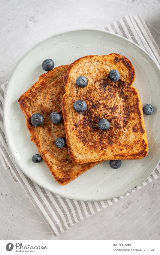 Close-up from above of three delicious slices of French Toast with blueberries on a plate on grey background, minimalistic style french toast wentelteefjes