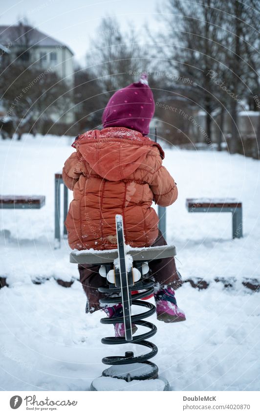 A child plays with a teeter-totter in the snowy playground Day Exterior shot naturally depth blur Life Joy Cold cold season Snow look away Winter chill 1