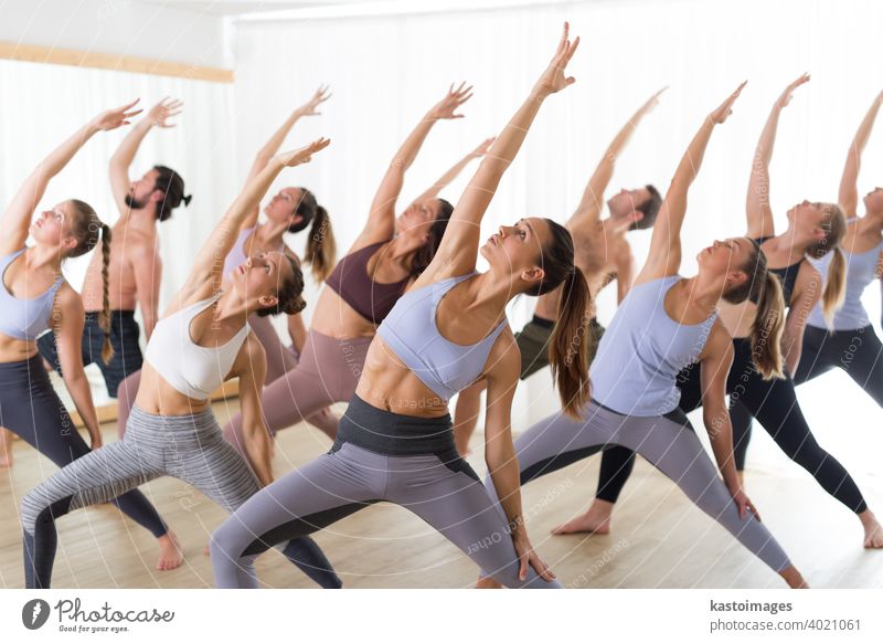 Group of young authentic sporty attractive people in yoga studio, practicing yoga lesson with instructor. Healthy active lifestyle, working out in gym class