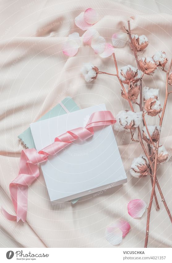 Aesthetic lifestyle. Notebook, white box with pink ribbon. Beige fabric background with cotton branches.  Top view. aesthetic notebook beige petals top view