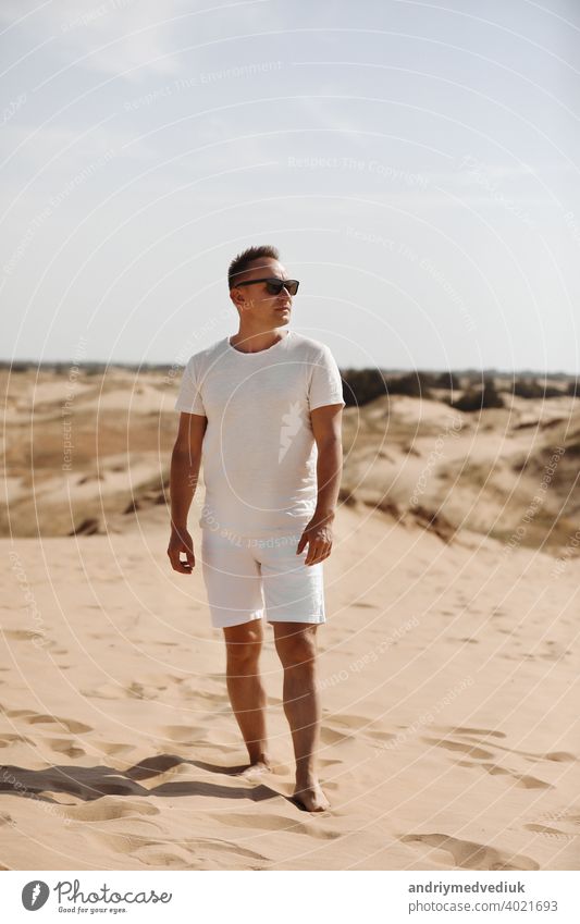 Young handsome man in light clothing and sunglasses in the desert. Concept of freedom relaxation. Place for text or advertising young concept person white