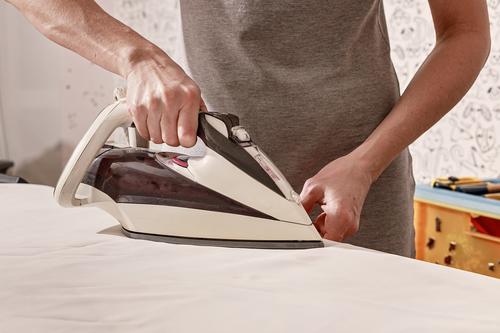 Hands of a caucasian woman holding an iron. Woman is ironing clothes on an ironing-board. Housework. Close-up. hands ironing board housework close-up grey