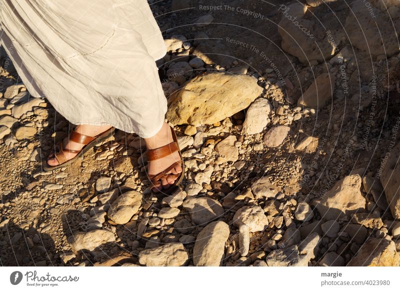A woman, girl with white skirt walks with comfortable sandals over a stony path Sandals Footwear feet find one's way Legs Feet Human being Woman Adults