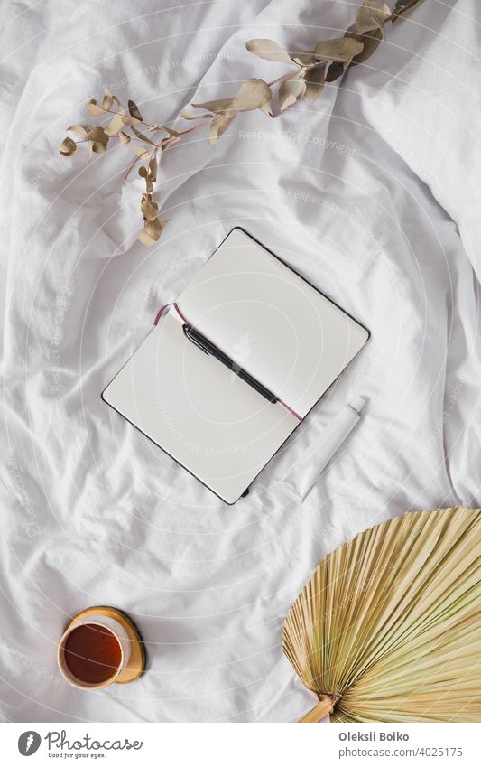Open notepad with blank pages in textile white background, dried flowers and cup of tea. Tranquil and mindful home living, staying in bed, hand writing in a note book concept