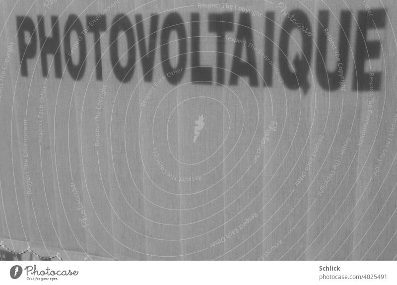 Shadow of the French inscription "PHOTOVOLTAIQUE" of a shop window falls on a closed inner blind with a lot of free space for text at the bottom Text