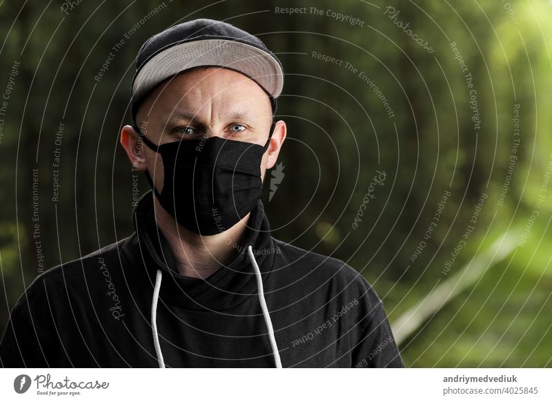 Young man in black protective antiviral mask in the summer park. The guy is resting outdoors on a sunny summer day in a mask made by his own hands. Virus protection. Quarantine measures