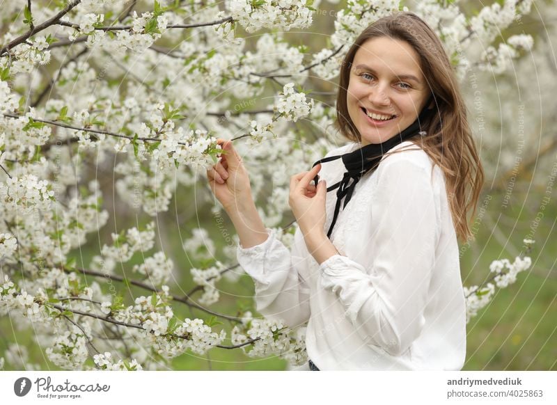 woman took off her mask to inhale the smell of flowers. girl touches the blossoming cherry tree branch in the garden with her hands on a spring day. beautiful girl in a cherry blossom.