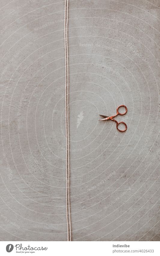 A small rose gold scissor and a piece of rope on grey background. yarn cut scissors hobby diy activity break closeup concept craft creative design divide