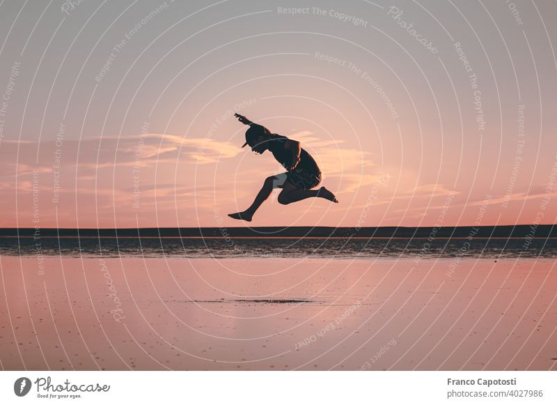 young man jumping on the beach Man Flying Freedom Sports Clouds Sky Jump Silhouette Lake Water Beautiful weather Summer Back-light Happiness pink sky Happy