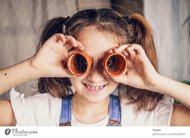 nice little girl is having fun using flowerpots as eyeglasses. child amusements, happy childhood moments. caucasian ethnicity. close-up kid beautiful face
