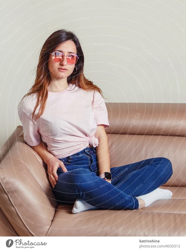 Young women sitting on the sofa at home wear mockup t-shirt sunglasses Lifestyle jeans indoor relax long hair couch round neck casual mock up Person Portrait