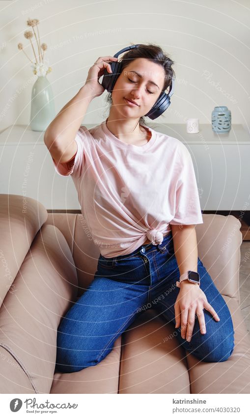 Young women listening to music with headphones wear mockup t-shirt Lifestyle jeans indoor sofa couch round neck casual mock up bun Person Portrait Human Female