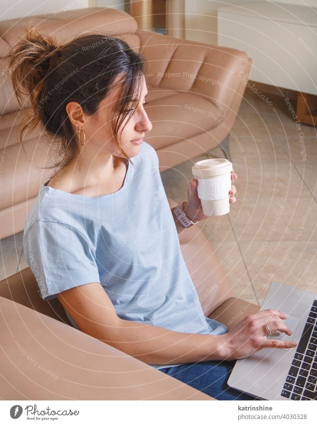 Young women working with laptop while sitting on the sofa at home wear mockup t-shirt learn student Lifestyle jeans coffee to go cup serious concentrated indoor