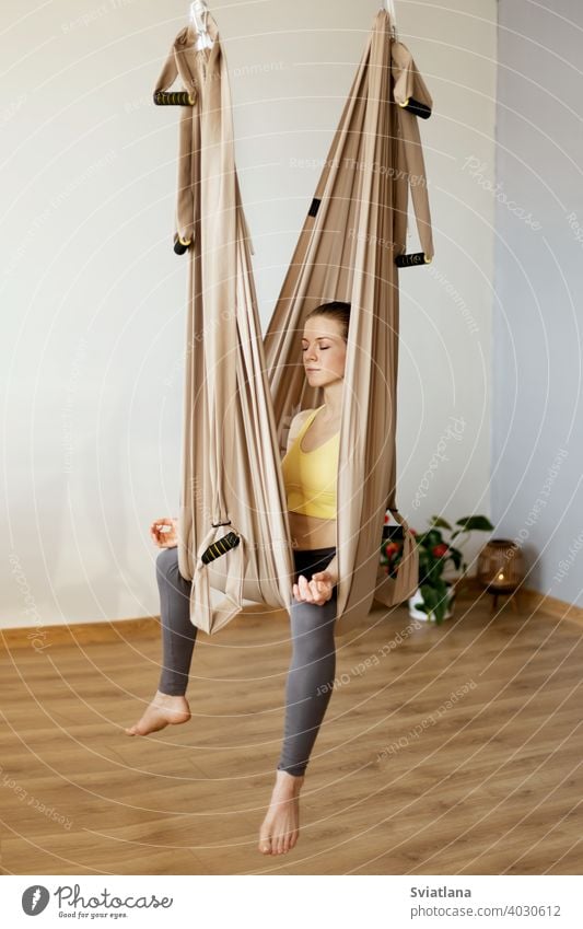 A young woman meditates while sitting in a hammock in a yoga class. Aero yoga, sports, healthy lifestyle fitness relax girl club meditation stretch pose aerial