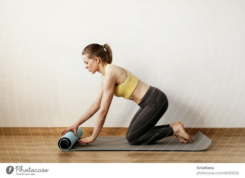 A young girl rolls out a yoga mat before taking a yoga class. Yoga, fitness, lifestyle pose standing woman body exercise studio extended side sport stretch