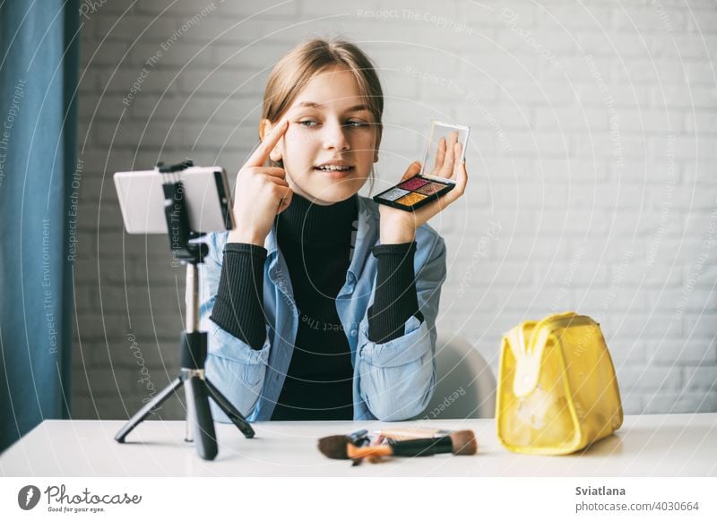 A teenage girl does makeup and shows how to apply blush while recording video for her blog on her smartphone on a tripod at home blogger camera cosmetics