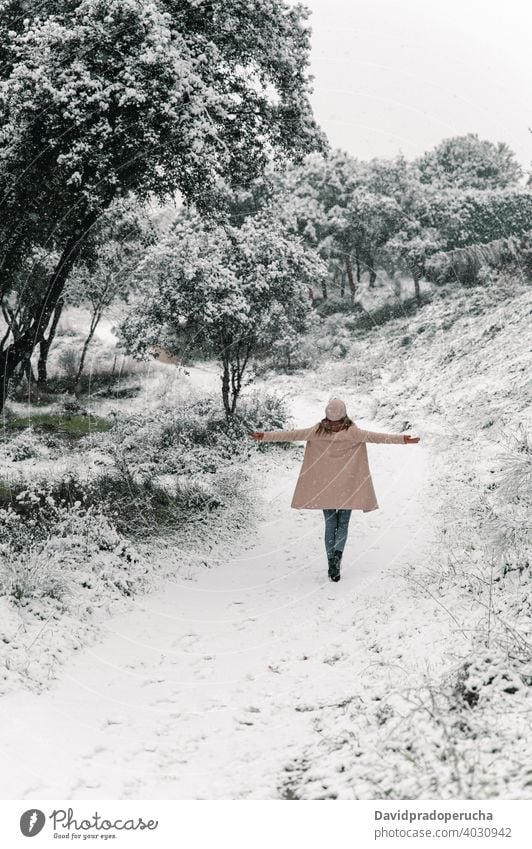 Unrecognizable woman walking in winter woods forest carefree outstretch enjoy stroll snow warm clothes wintertime weekend freedom hat coat season tree pathway