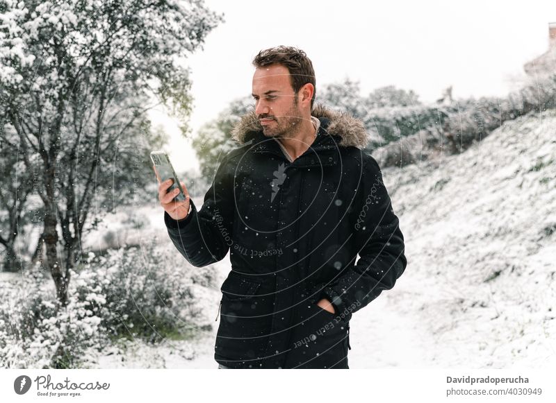 Man browsing smartphone in winter forest snowfall using warm clothes woods handsome outerwear cold connection mobile internet communicate nature device gadget