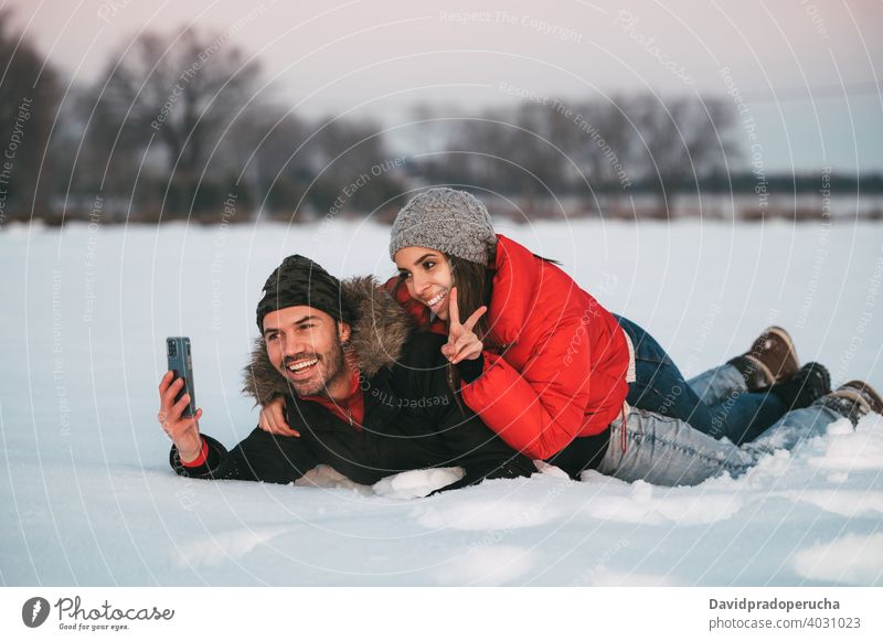 Laughing couple taking selfie on snow winter having fun cheerful countryside love together smartphone joy laugh field romantic relationship affection excited