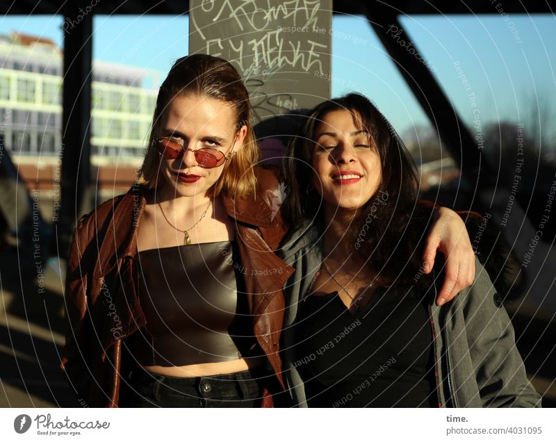 Lara and Estila Woman Long-haired Stand Earnest Cool Friendship Coat Easygoing Blonde Dark-haired Architecture Bridge sunny Sunlight togetherness