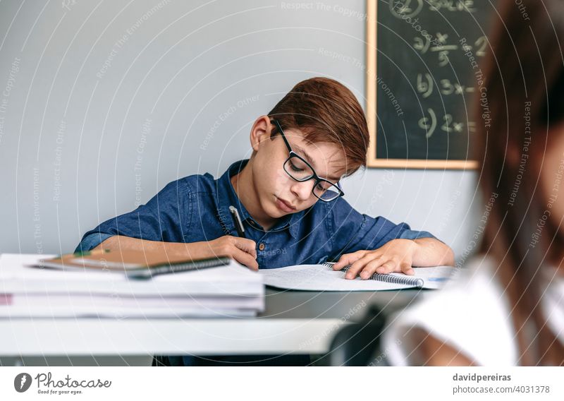 Boy writing in notebook at school boy student classroom education studious people young girl teen female two person child kid children caucasian glasses