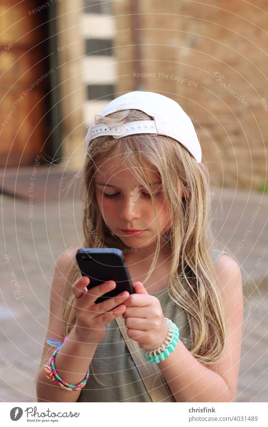 Girl in cap looks at mobile phone Child teen youthful Media Consumption peril media society Addiction Cellphone Electronics Internet Mobility Chat social media