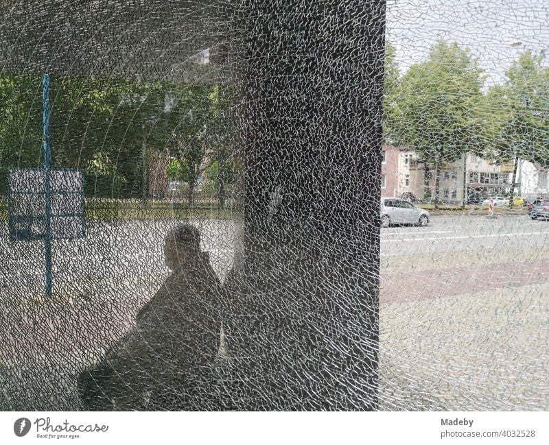 Sitting man behind the shattered glass of a bus stop in front of the Kunsthalle Bielefeld in the Teutoburg Forest in East Westphalia-Lippe