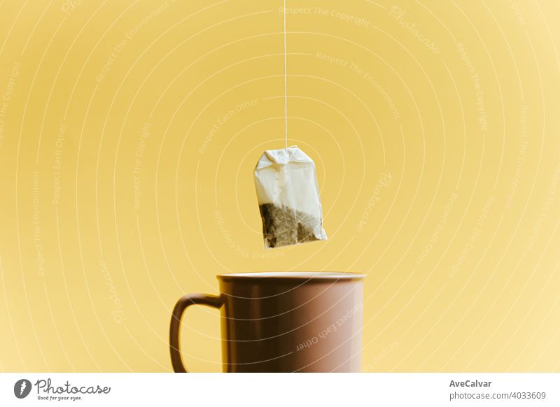 A super minimalistic shot of a bag of fast tea over a pink cup over a pastel yellow background conceptual copy-space marketing sparse temptation tranquility