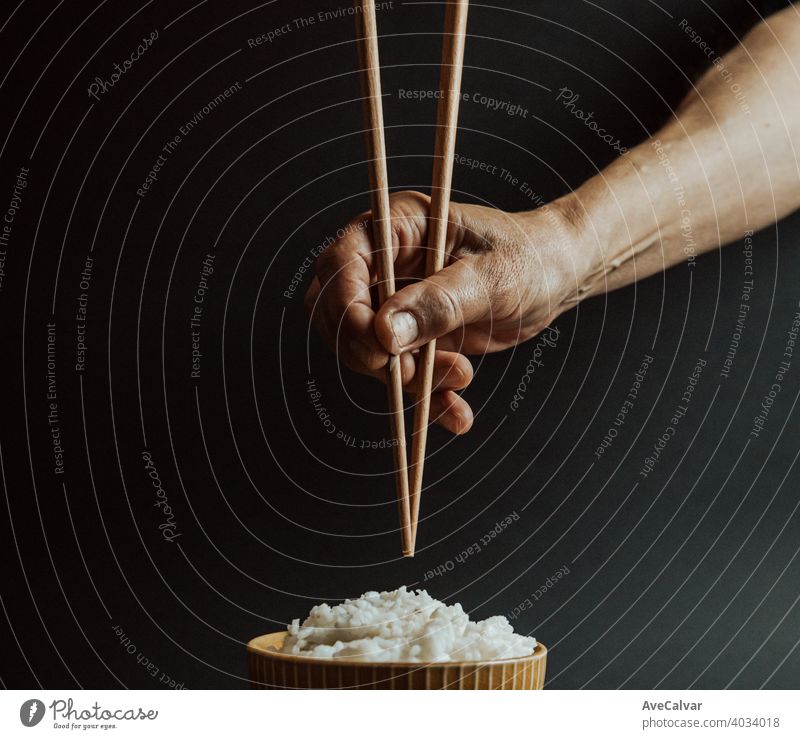 Minimalistic old hands grabbing japanese chopsticks over a bowl of rice concept shot on cinematic tones over a black background minimal copyspace dark