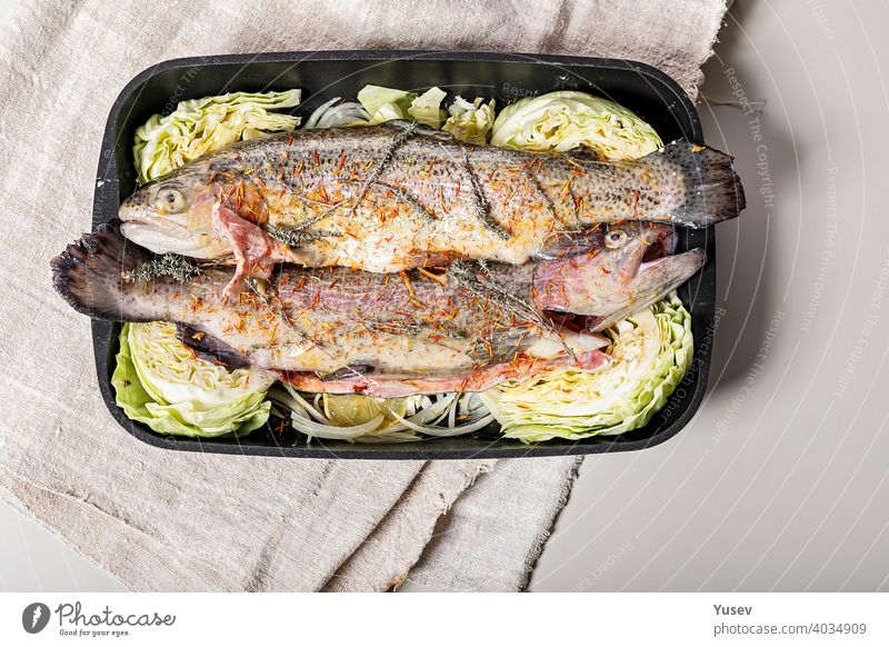 Fresh trout with spices and vegetables. Freshwater fish with saffron, red onion and cabbage in a cast iron baking dish. Light background. Top view. Copy space