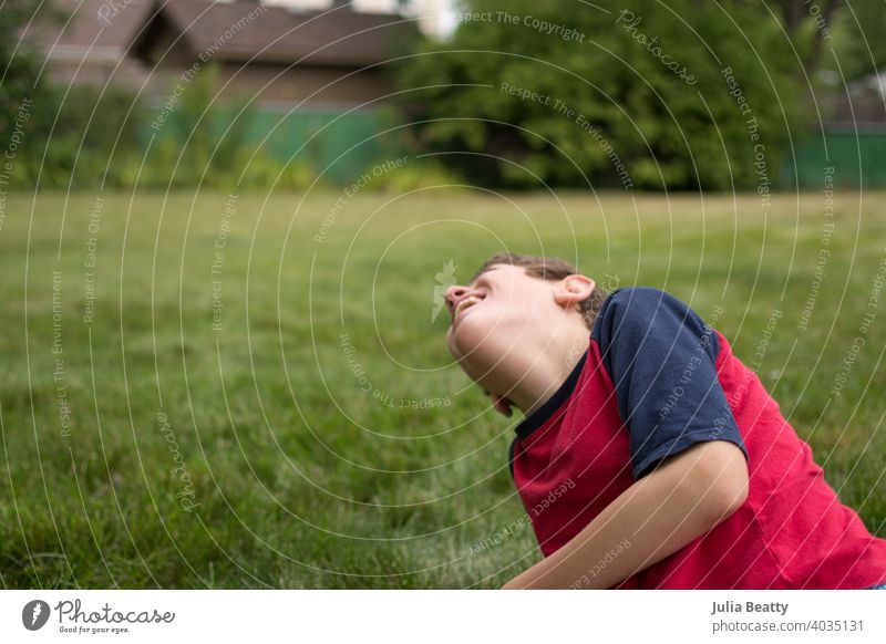 Boy with Autism laughing while sitting in the grass in his backyard; summertime fun special needs autism communicate communication autism awareness