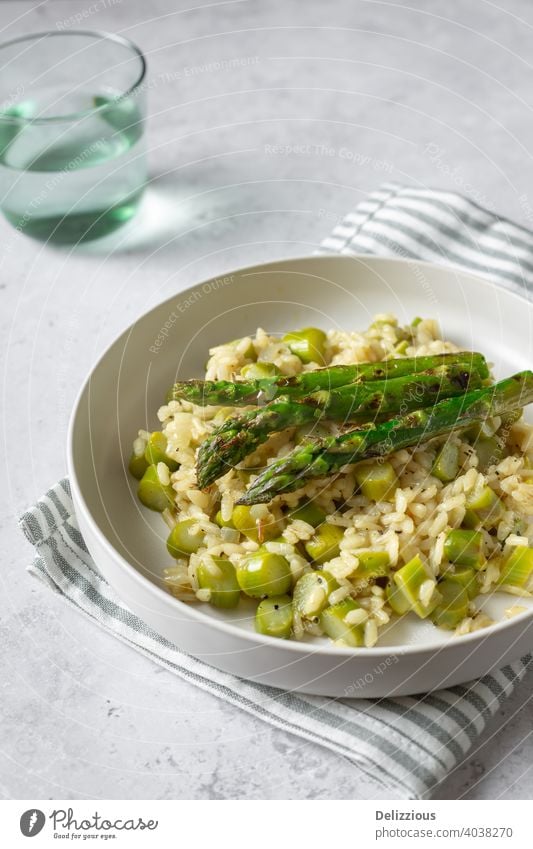 Tasty risotto with grilled asparagus on white plate, grey background, vertical with green glass green asparagus food side view recipe cooking home made chef