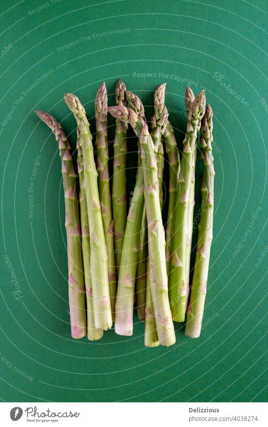 A bundle of fresh green asparagus on a green background, copy space, vertical vegan flat lay cooking ingredients food healthy vegetarian raw clean ready-to-eat