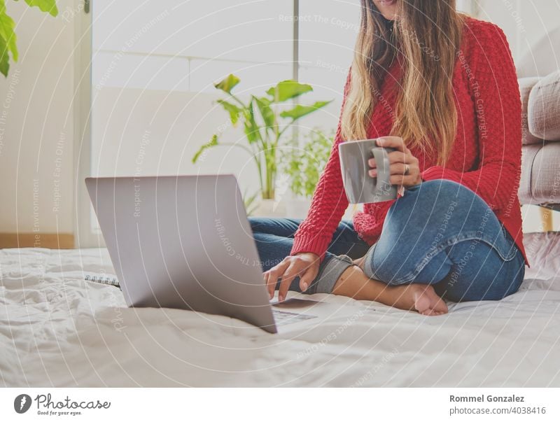 A woman having tea, sitting on the floor of an apartment, jotting down notes, opened a laptop in front of her. Home office concept. Offering coffee. Concept creative work at home. Selective focus.