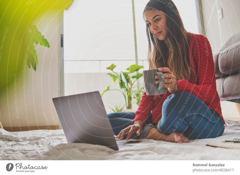 A woman having tea, sitting on the floor of an apartment, jotting down notes, opened a laptop in front of her. Home office concept. Offering coffee. Concept creative work at home. Selective focus.