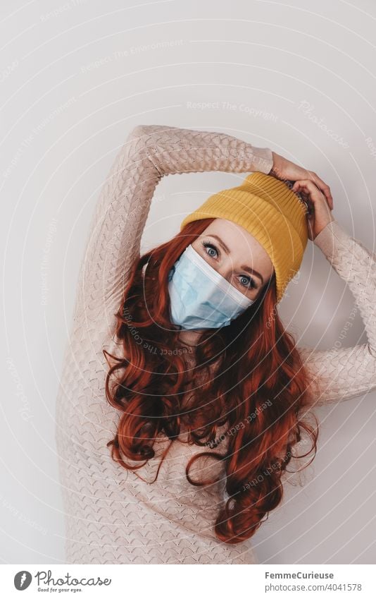 Young redhead woman in yellow hipster beanie cap and medical protection mask posing with both arms over head pose Red-haired curly hair Woman Young woman