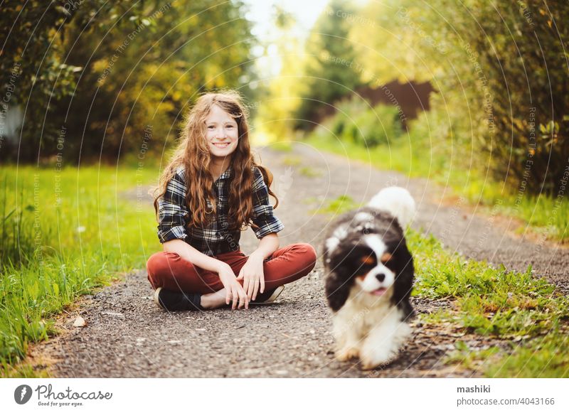 happy kid girl walking with her cavalier king charles spaniel dog on summer country road. Training her puppy and having fun. child animal pet nature outdoor