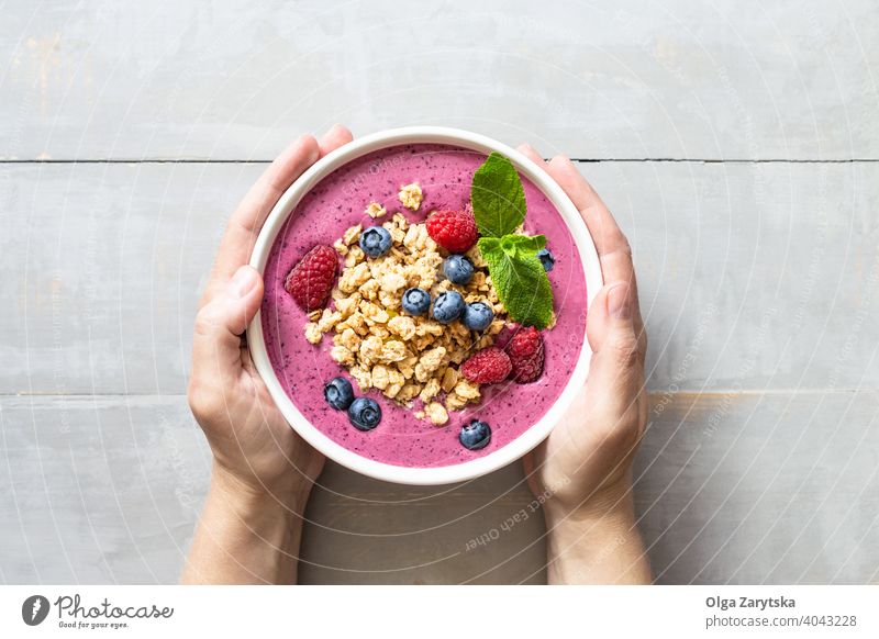 Female's hands holding smoothie bowl with granola and berries. breakfast healthy blueberry raspberry table yogurt top view vegan pink colorful food background