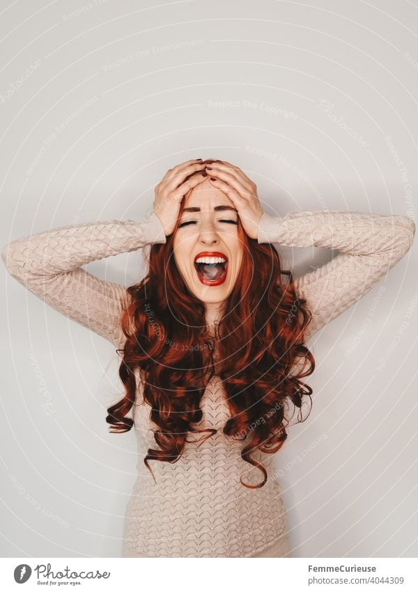 Woman with long red curly hair slaps both hands together over her head and screams red lips Scream Loud Red-haired red hair long hairs Feminine