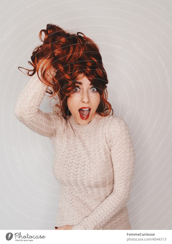 Woman holding her long curly red hair up with one hand and posing with her mouth open Neutral background Copy Space top Copy Space left Copy Space right